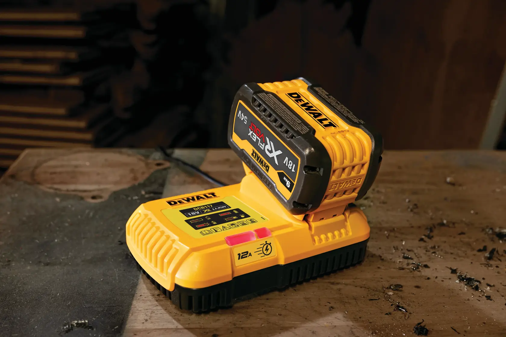 A DEWALT DCB117 yellow battery charger with an attached DEWALT XR FLEXVOLT 18V/54V battery, sitting on a dusty workbench.