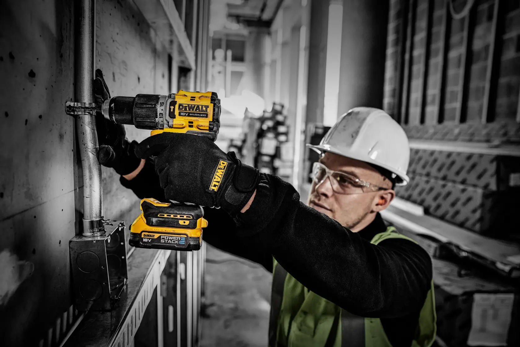 Worker uses DEWALT Powerstack battery in a cordless drill during electrical installation on an industrial site.