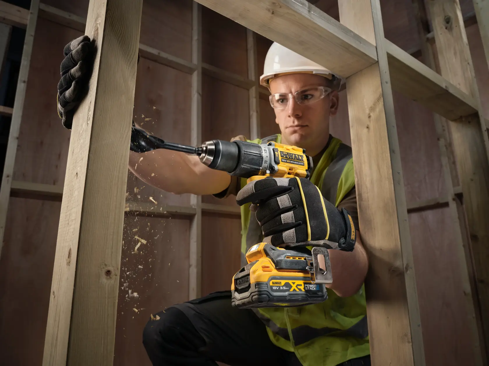Worker drills wood beam using a DEWALT cordless drill, wearing gloves and safety gear at a construction site.