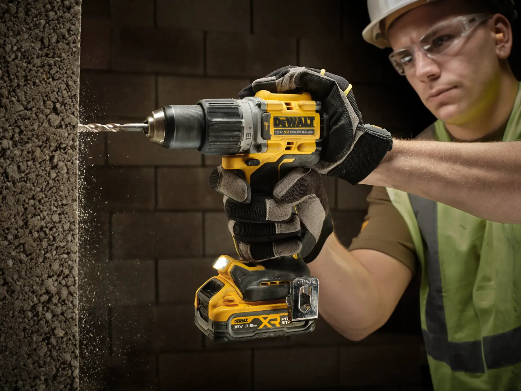 Gloved person uses a DEWALT cordless drill to bore into a concrete wall, with dust visible around the drill bit.