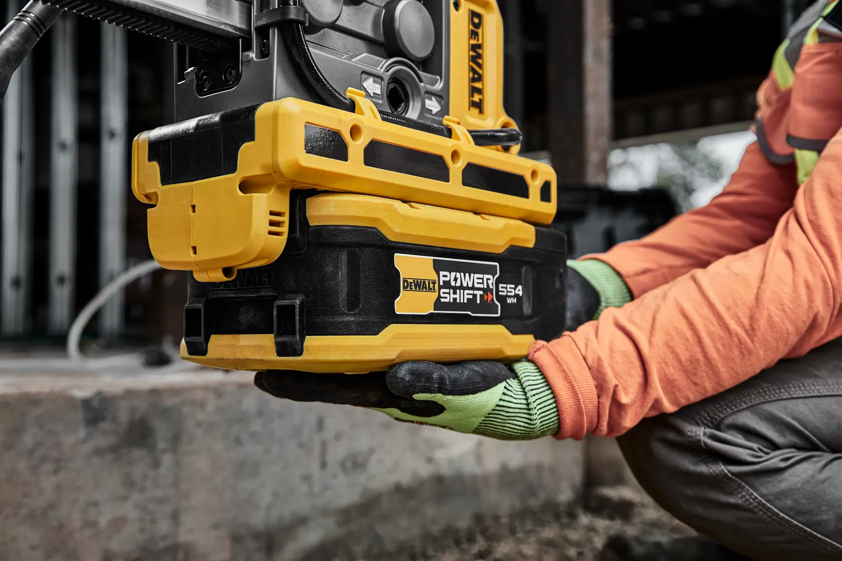 DEWALT Power Shift DCBPS0554 battery held by a worker in gloves at a construction site.