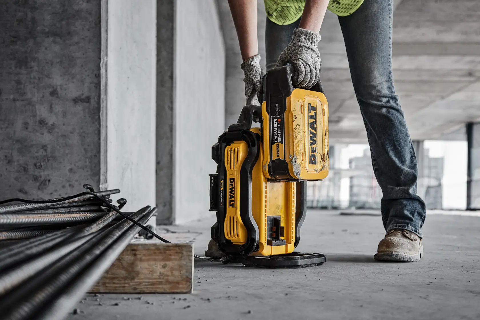 Person uses a yellow DEWALT battery pack on a construction site with tools and metal bars nearby.
