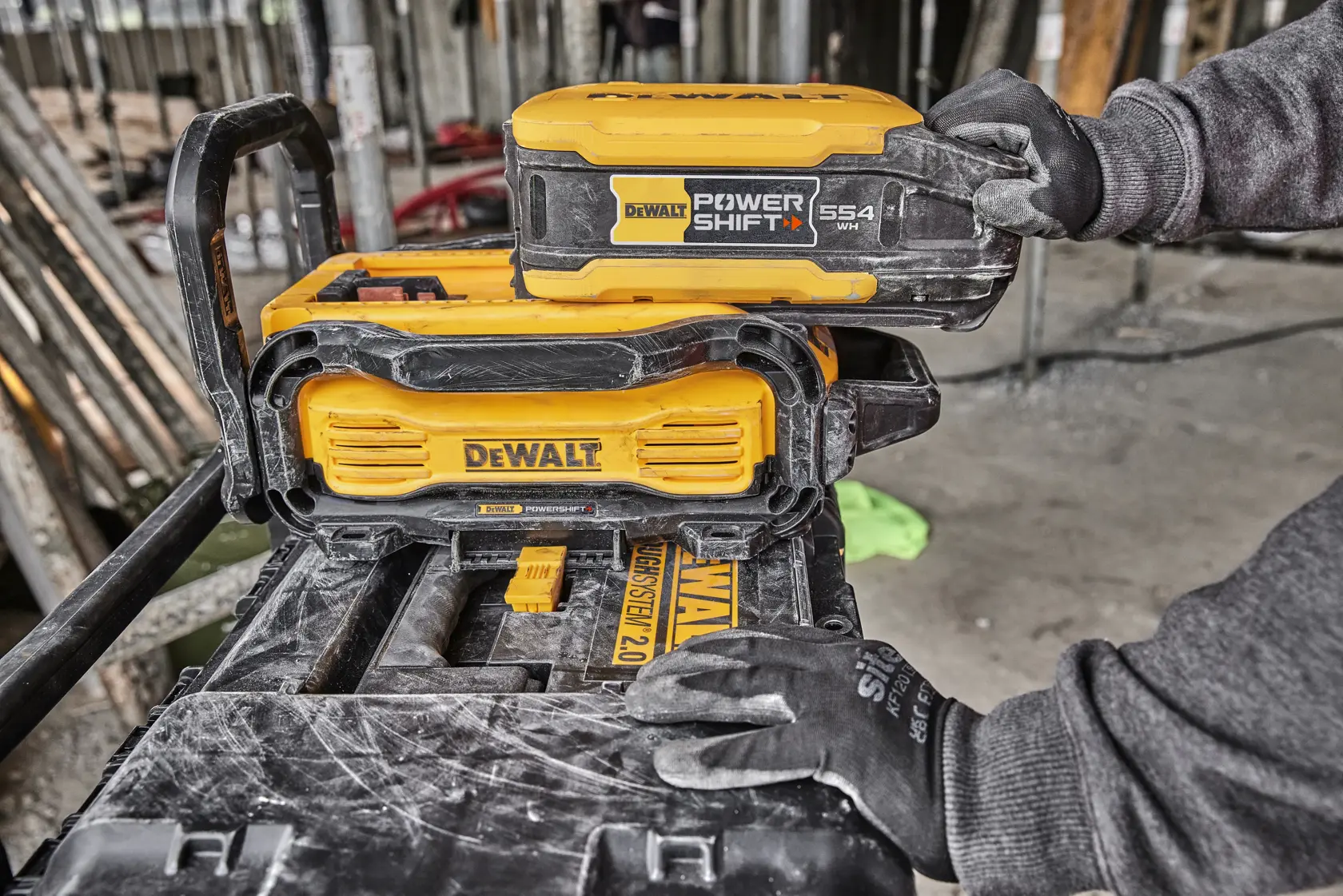 DEWALT Power Shift battery being placed in a yellow DEWALT device at a construction site, handled by a gloved hand.