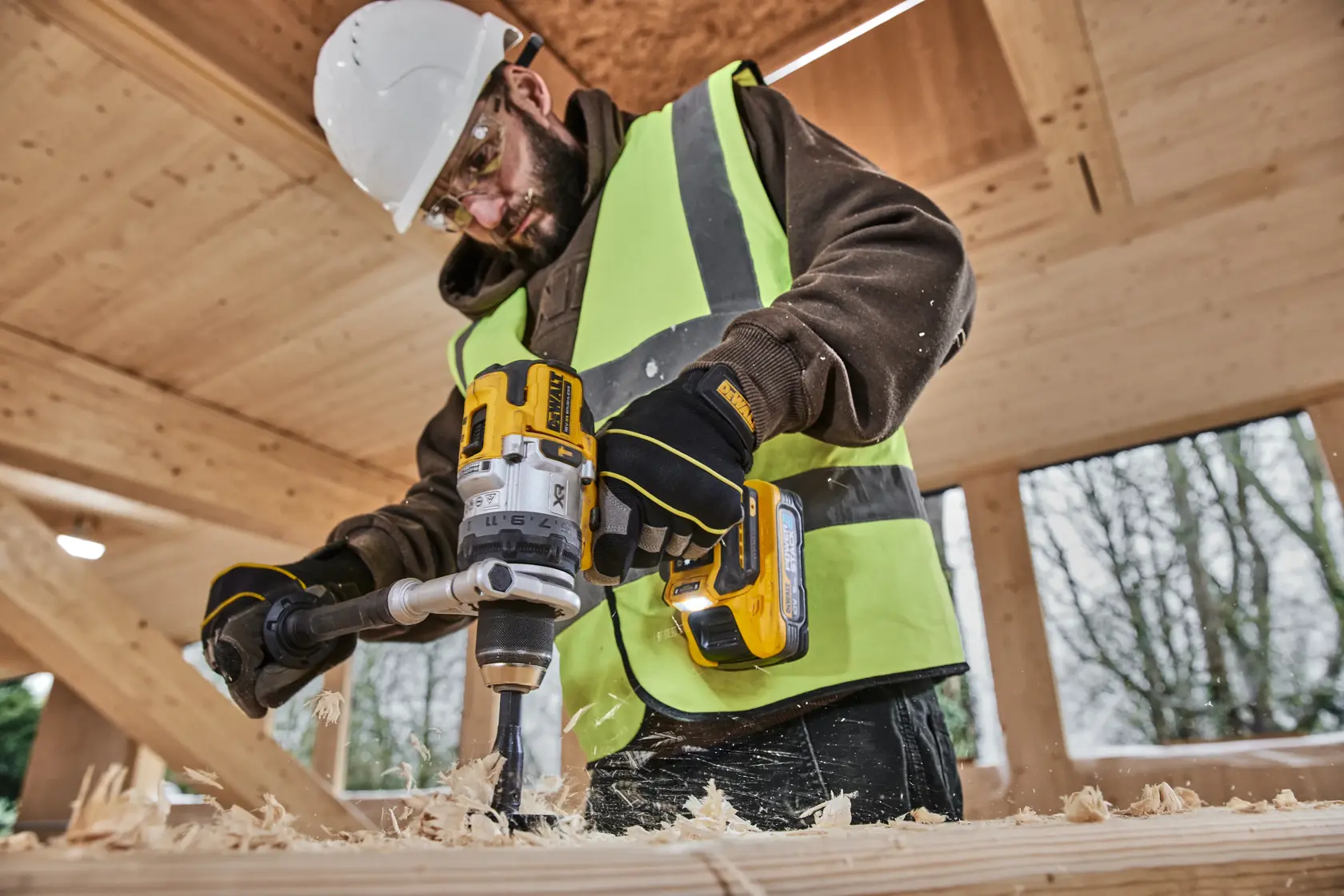 Worker uses DEWALT DCD1007NT and DCZ607X2-XE drills on wood. Photography product category. Safety gear worn.