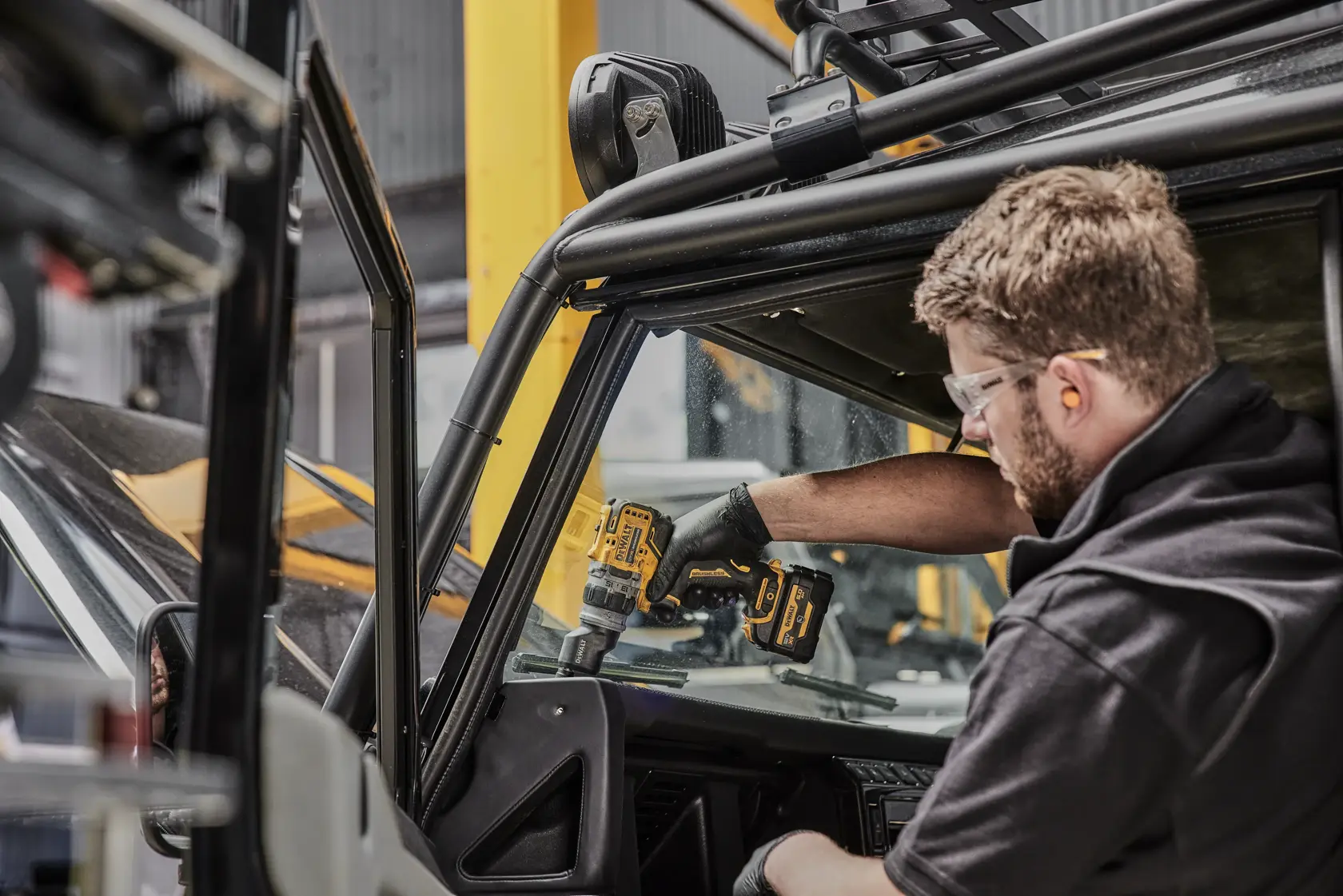 A person using a DEWALT cordless drill inside a vehicle, working on the dashboard area. The person’s face is blurred for privacy.