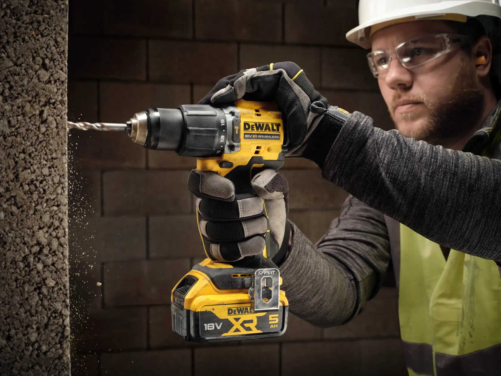 Gloved hand using a DEWALT cordless drill to drill into a concrete wall, construction setting visible.