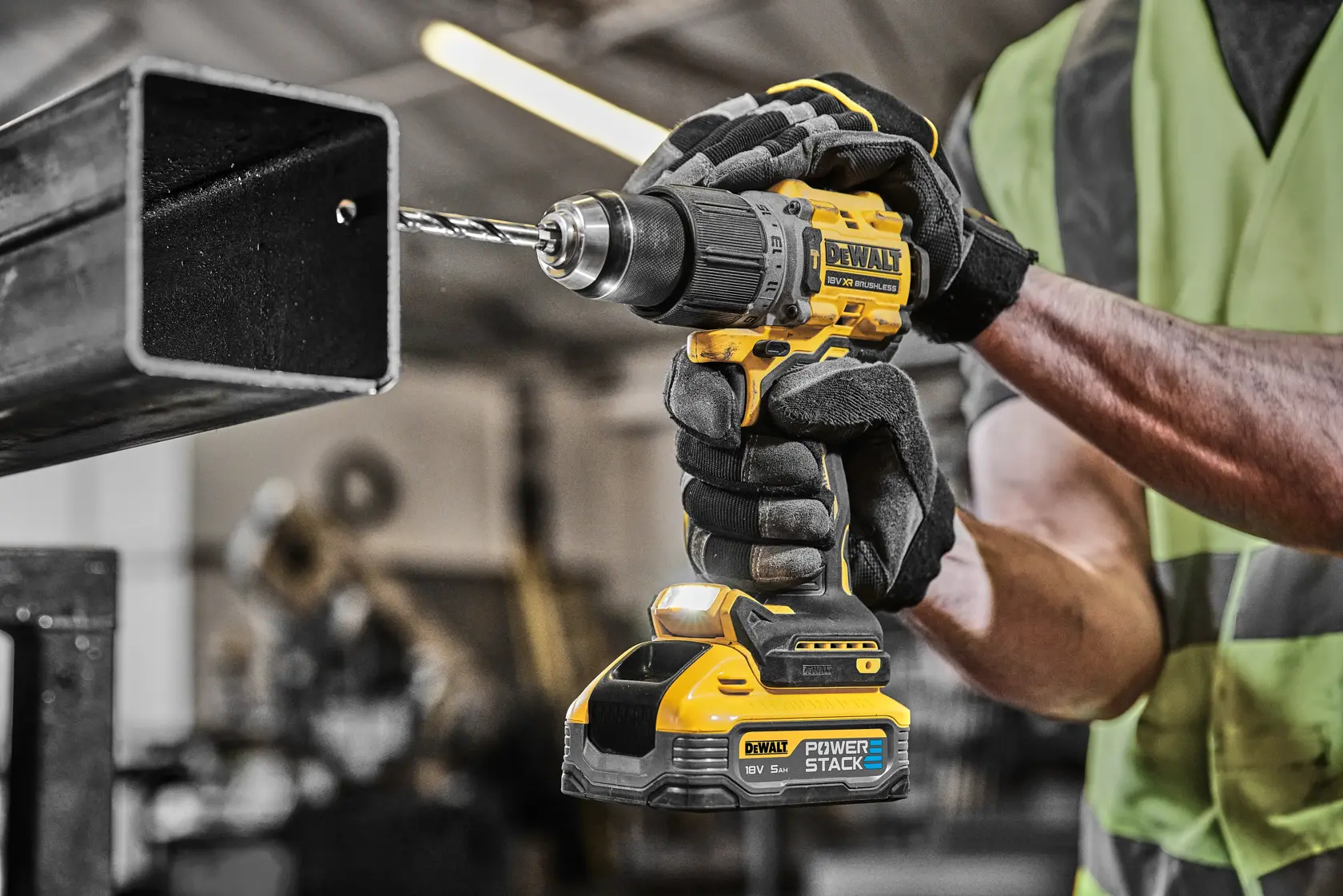 Gloved worker drills metal using a yellow DEWALT cordless drill in an industrial workshop.