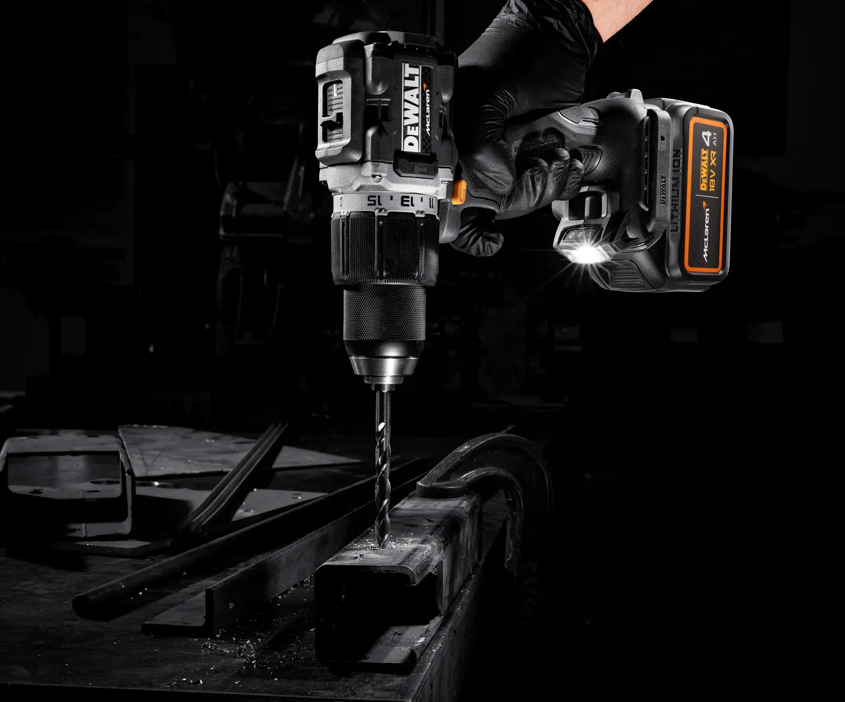 DEWALT cordless drill in use drilling metal with a gloved hand, LED light activated, in a dark workshop setting.