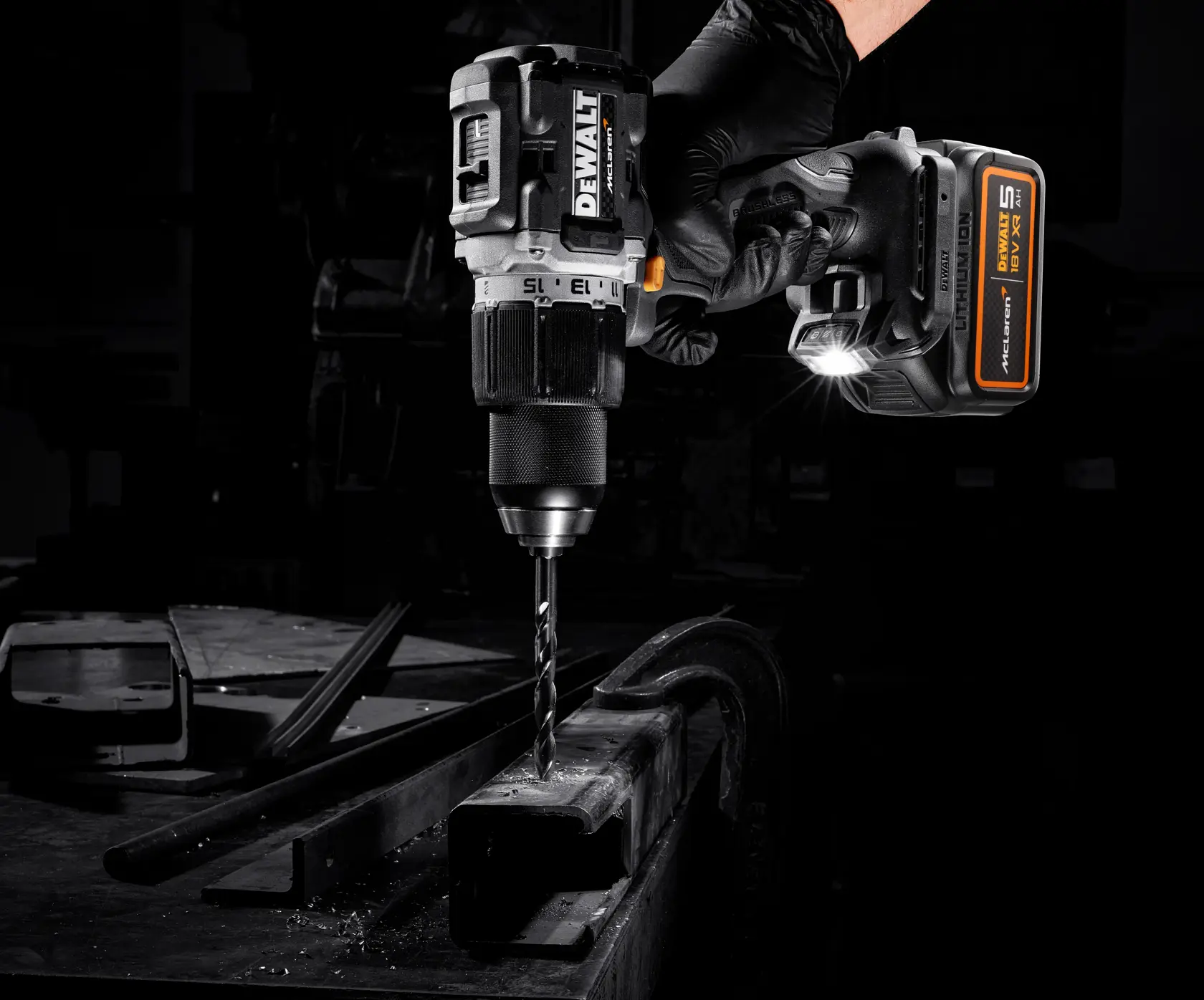 DEWALT cordless drill in use on metal, held by a gloved hand with LED light illuminating the work area.
