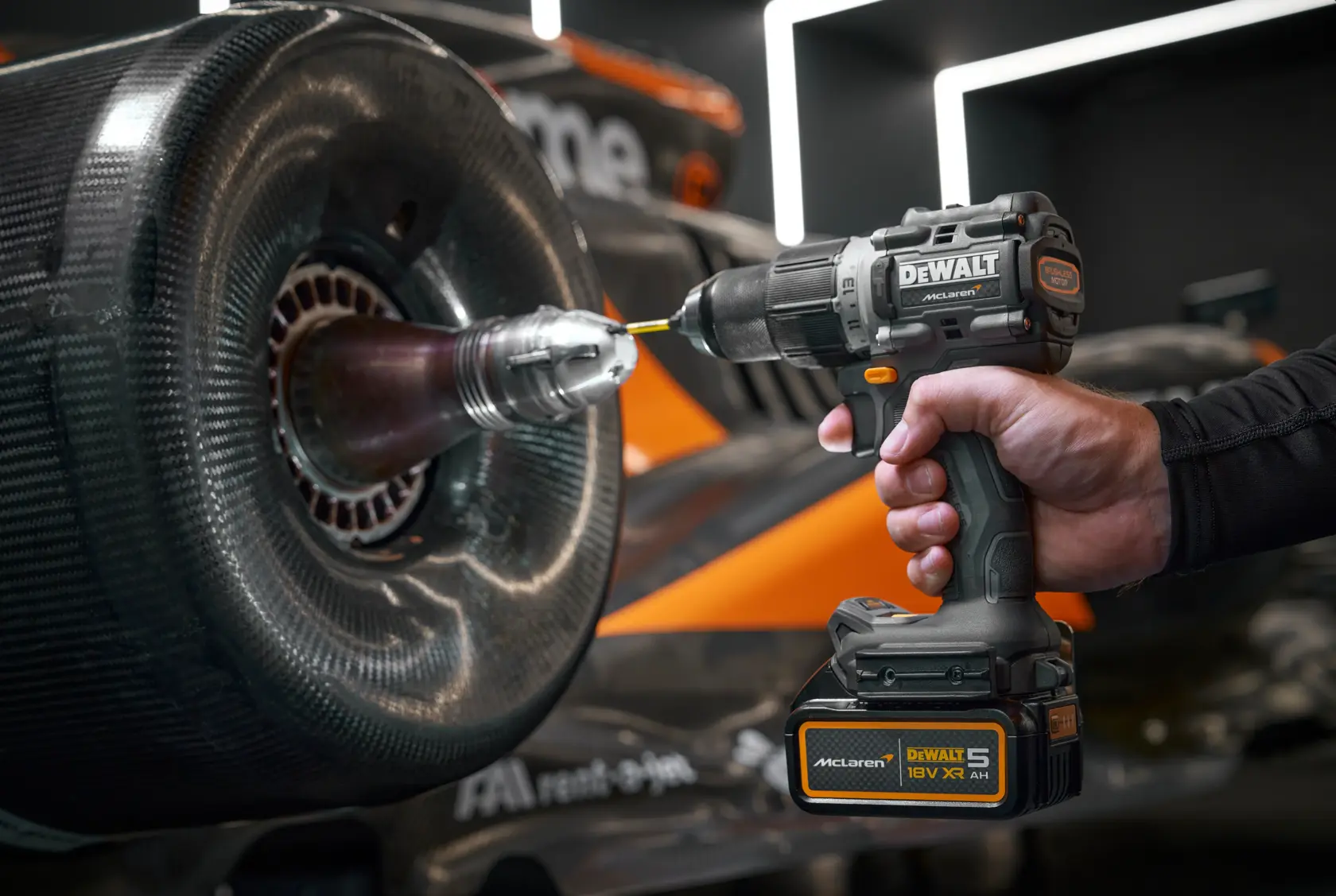 Hand using DEWALT cordless drill on a race car wheel. McLaren branding is visible on the tool.