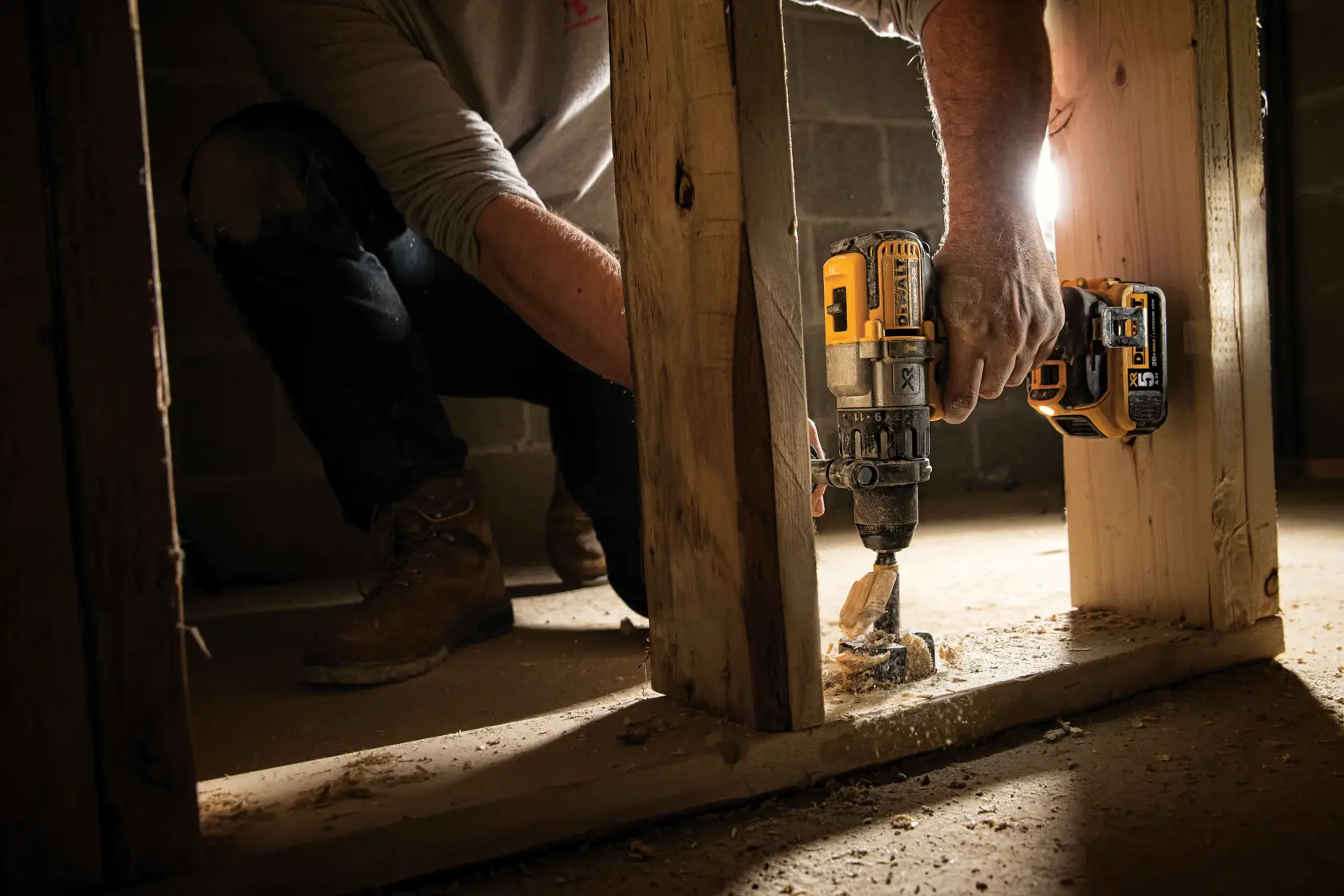 A person using a DEWALT cordless drill (model DCD996P2) to drill into a wooden beam at a construction site.