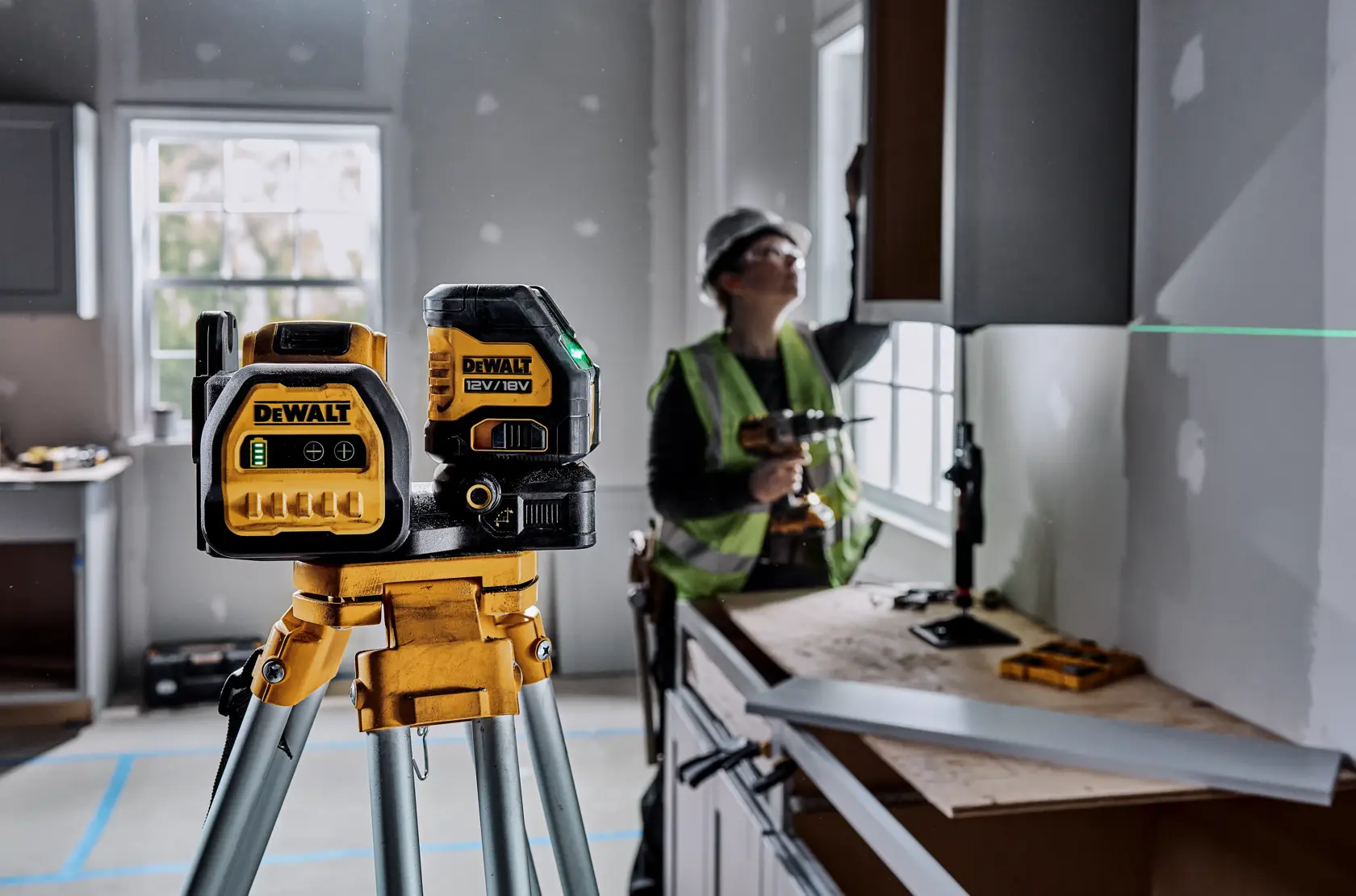 DEWALT laser tool (DCE088D1G18-QW, DCE088D1G18) in use at a construction site on tripod, worker in background.