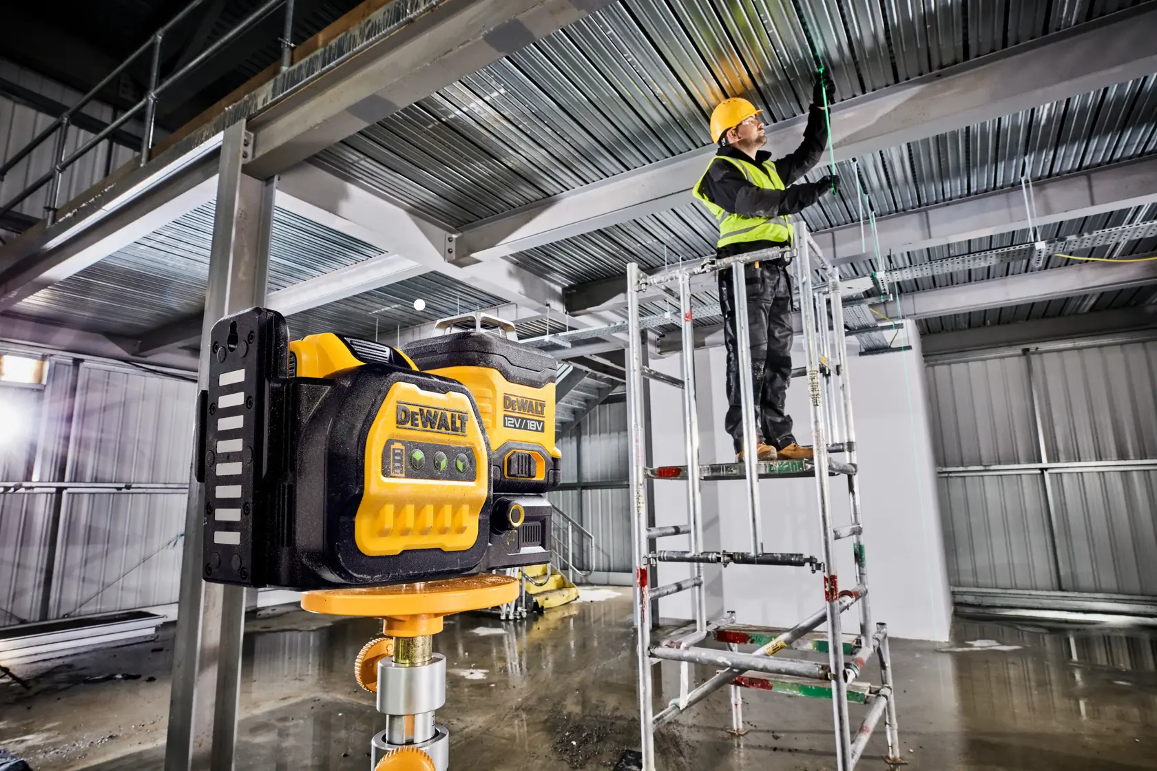DEWALT laser tool in use at a construction site inside, worker on scaffold adjusting ceiling wiring.
