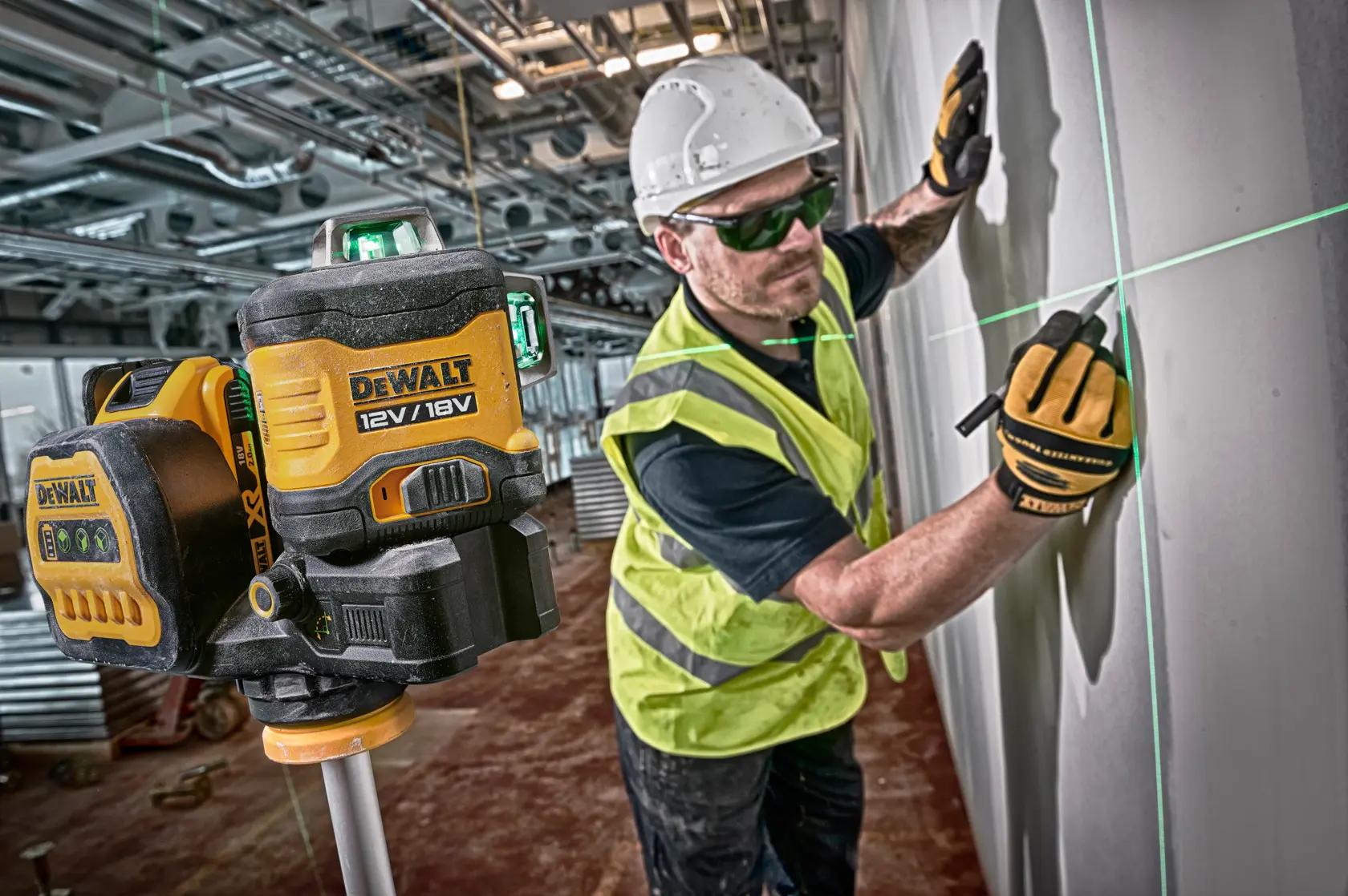 DEWALT laser level projects green lines on wall, worker marks alignment wearing gloves and hard hat at construction site.