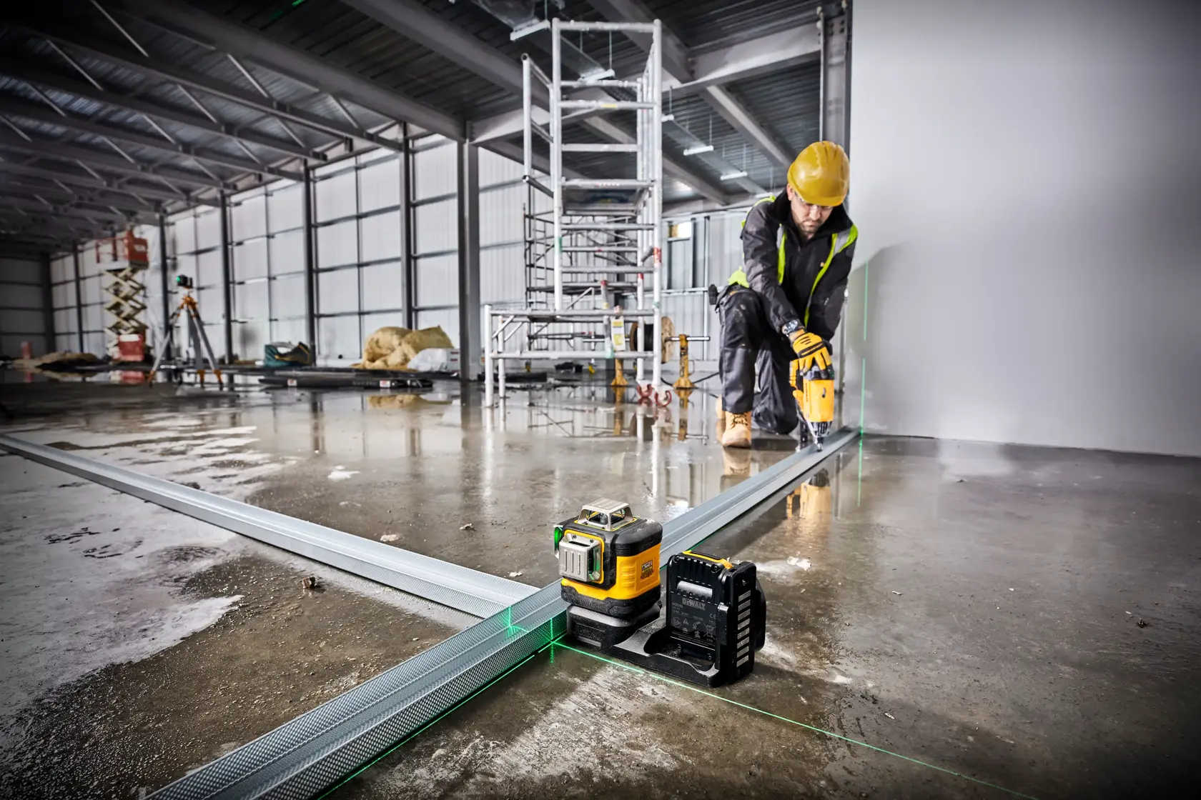 DEWALT laser level in use at a construction site, worker in safety gear aligning metal framing on a wet floor.