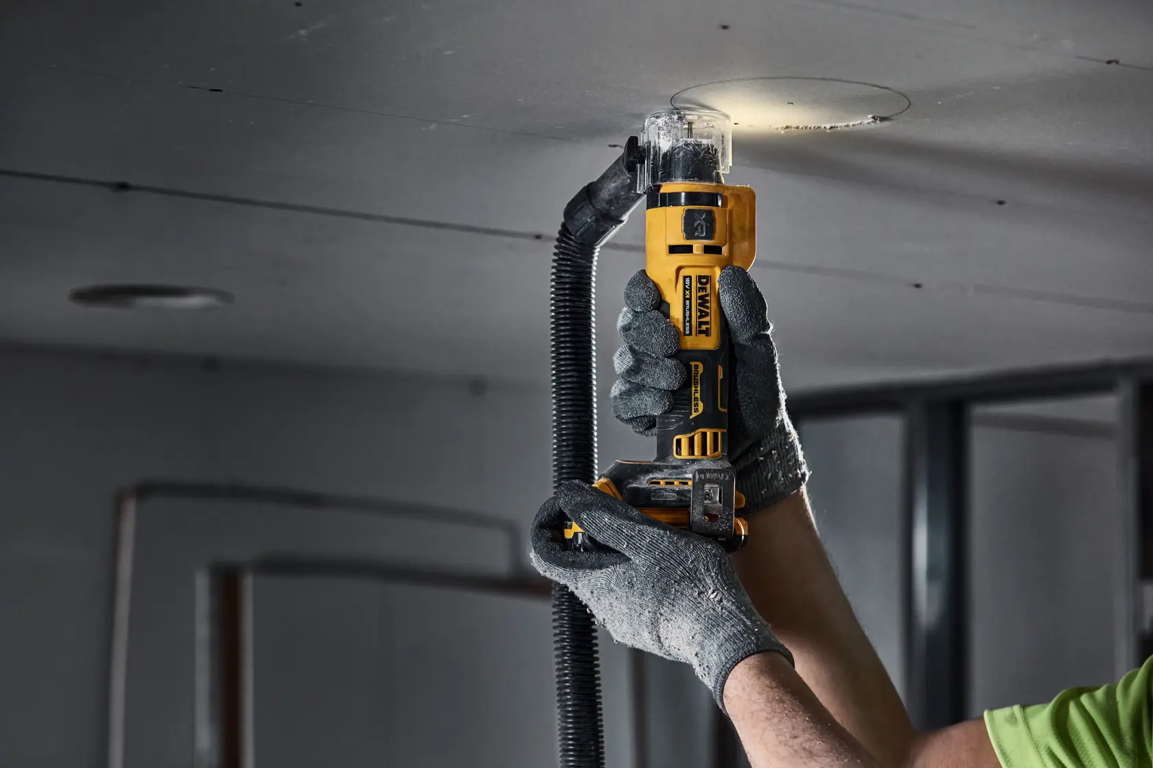 Hand using DEWALT drywall cut-out tool to cut a circular hole in a ceiling panel.