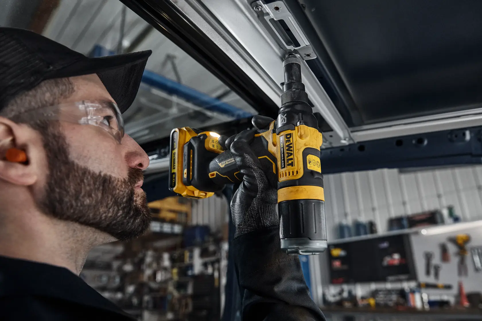 En person bruker en DEWALT DCF403NT batteridrevet skrutrekker for å feste en skrue i en metallramme på et verksted. Fokuset er på verktøyet og brukerens hanskekledde hånd.