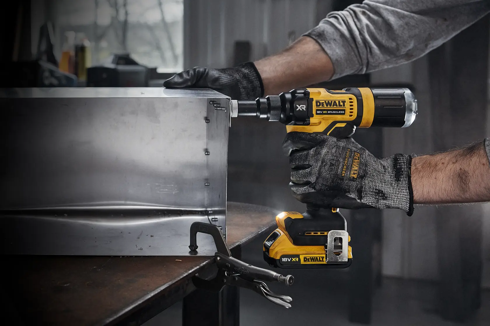 En person med arbeidshansker bruker et DEWALT DCF403NT trådløst elektrisk verktøy til å feste skruer i en metallboks i et verksted.