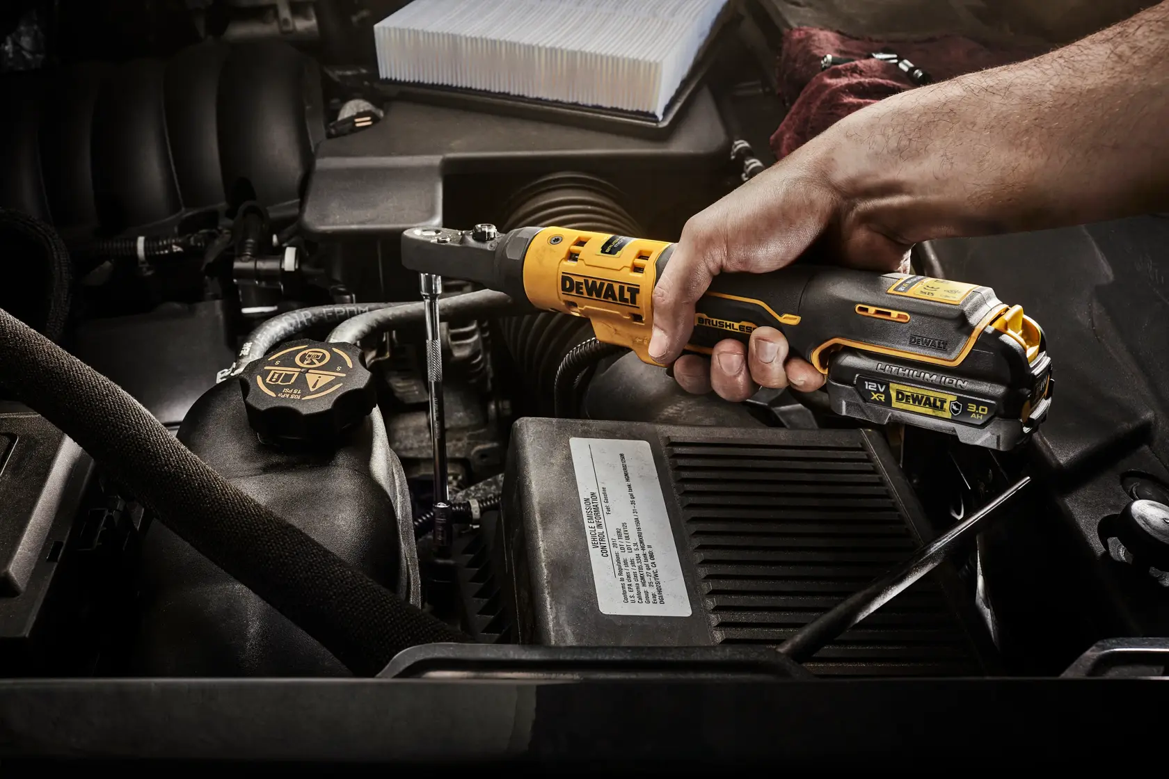 Hand using a DEWALT cordless ratchet DCF500N on a car engine for maintenance work.