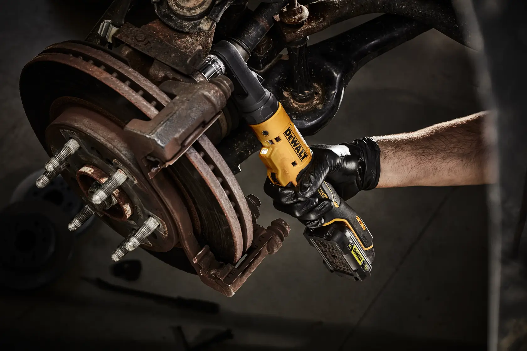 Person uses DEWALT cordless ratchet tool to work on a car's brake assembly, wearing black gloves.