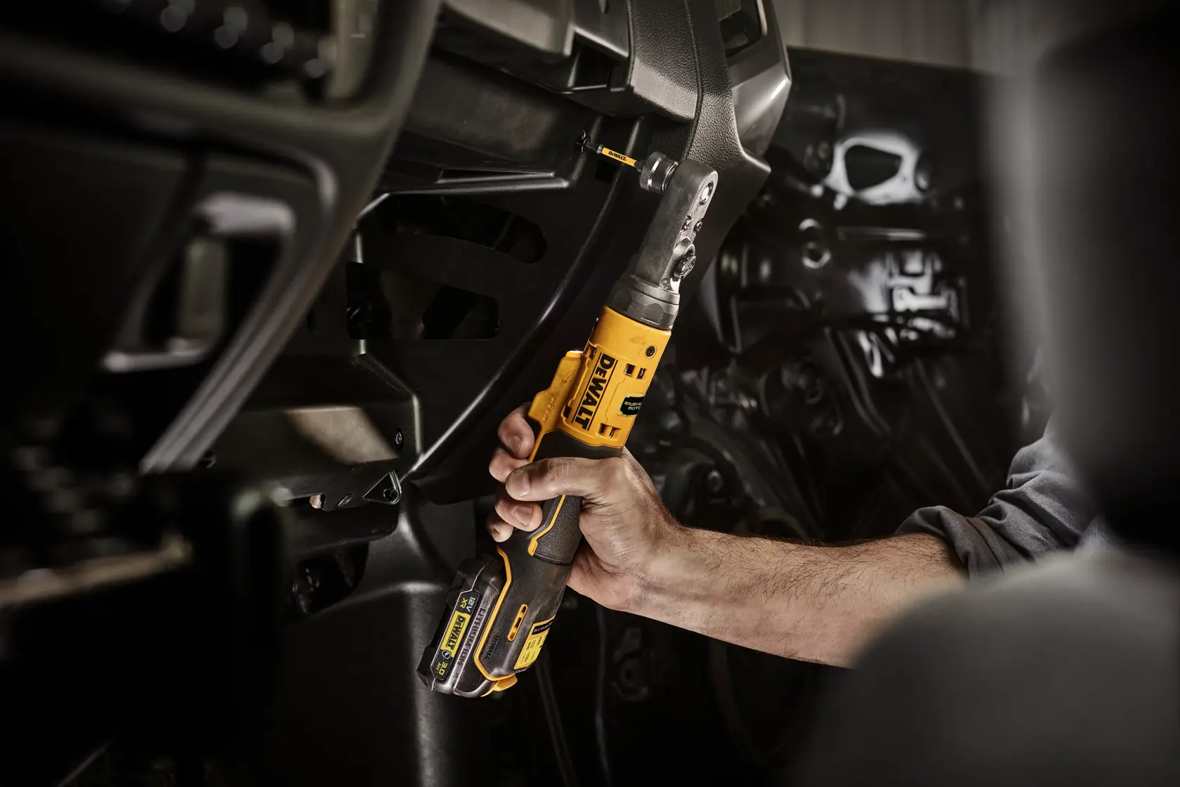 Hand uses DEWALT cordless ratchet tool to work inside a vehicle dashboard area.