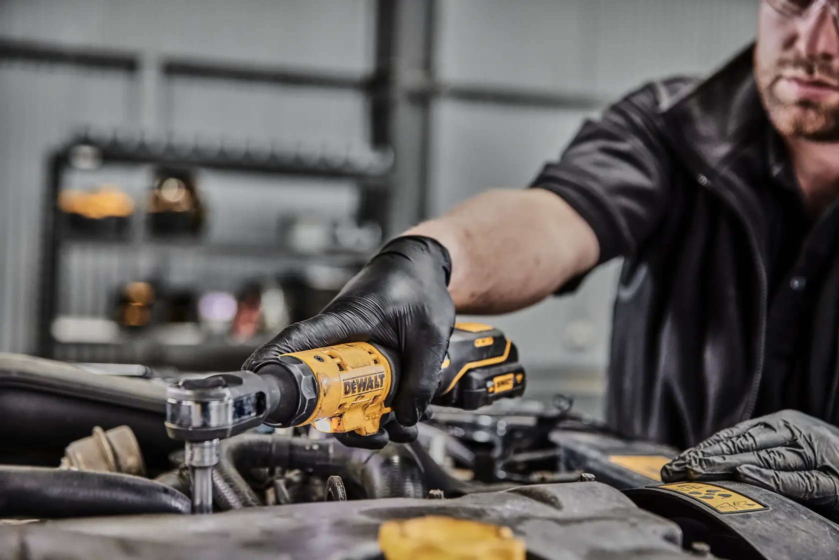 Una persona con guanti neri utilizza un cricchetto senza fili giallo DEWALT per lavorare su un motore in un'officina.
