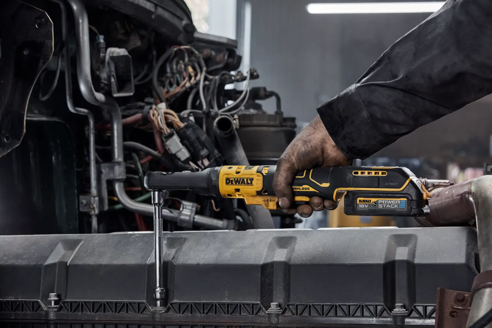 Person using a DEWALT cordless ratchet tool to tighten a bolt on a vehicle engine part.