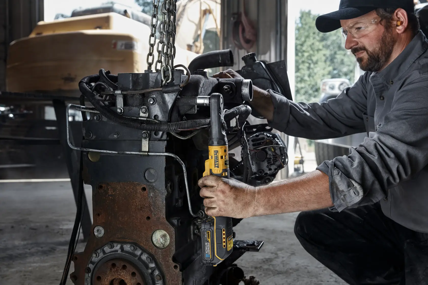 Person uses DEWALT cordless ratchet tool on machinery part in workshop setting.