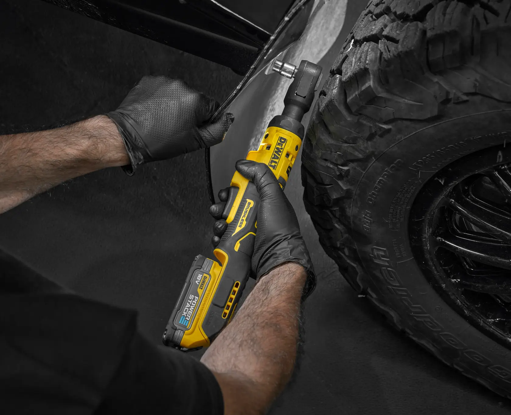 Person uses a DEWALT cordless ratchet near a car tire, wearing black gloves for precision work.