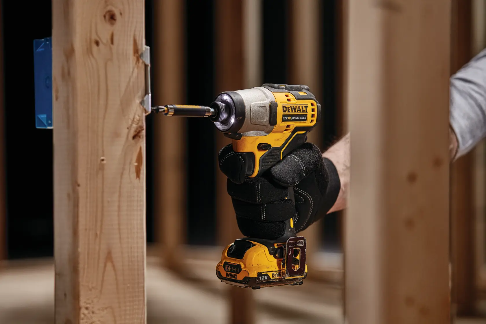 Gloved hand using DEWALT DCF601N power tool to drill into wooden frame.