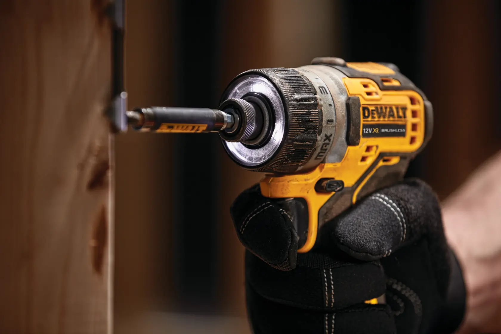 A DEWALT cordless screwdriver being used to drive a screw into wood, held by a gloved hand.
