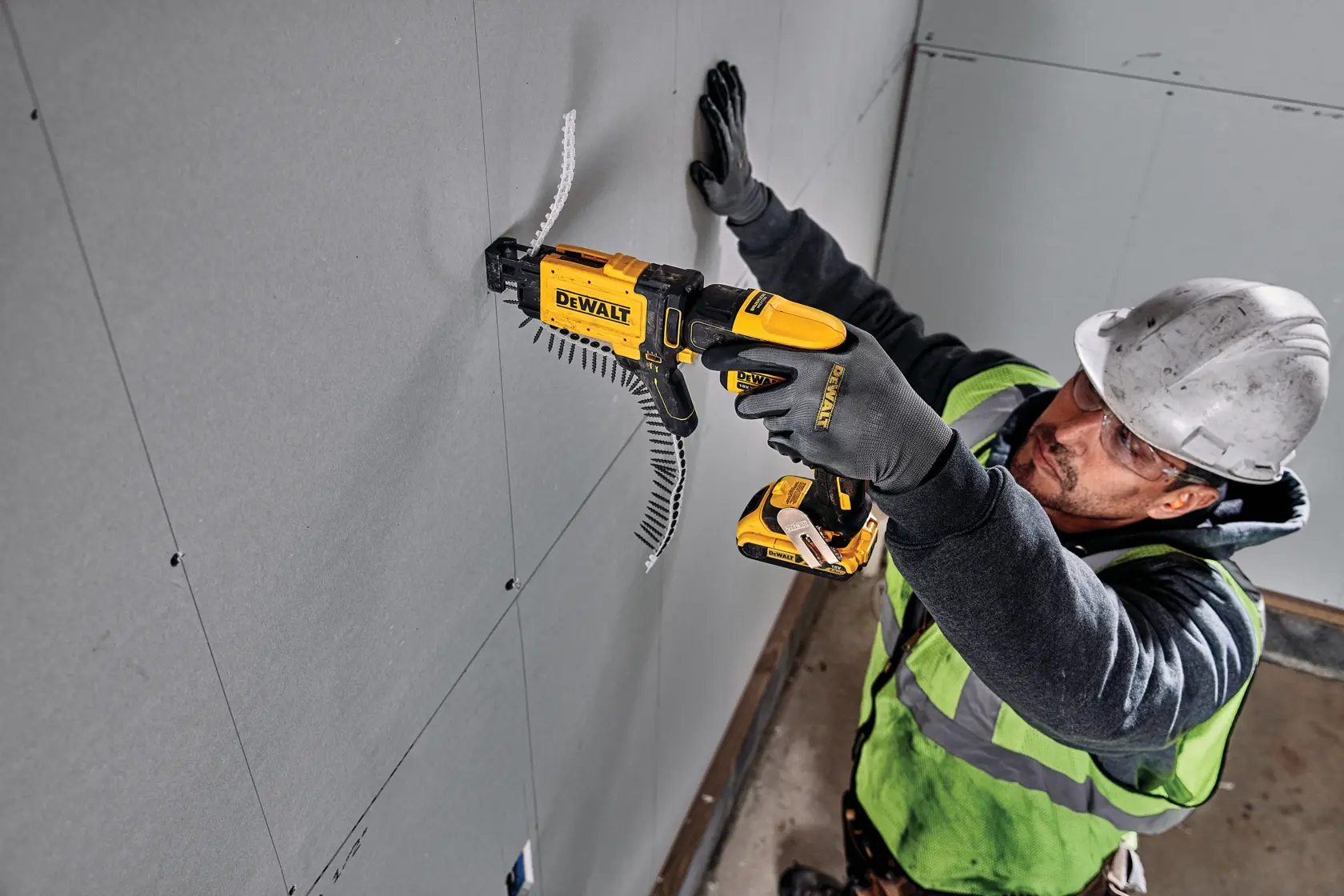 Person using a DEWALT DCF6202 screw gun to attach drywall panels at a construction site. Face is blurred for privacy.