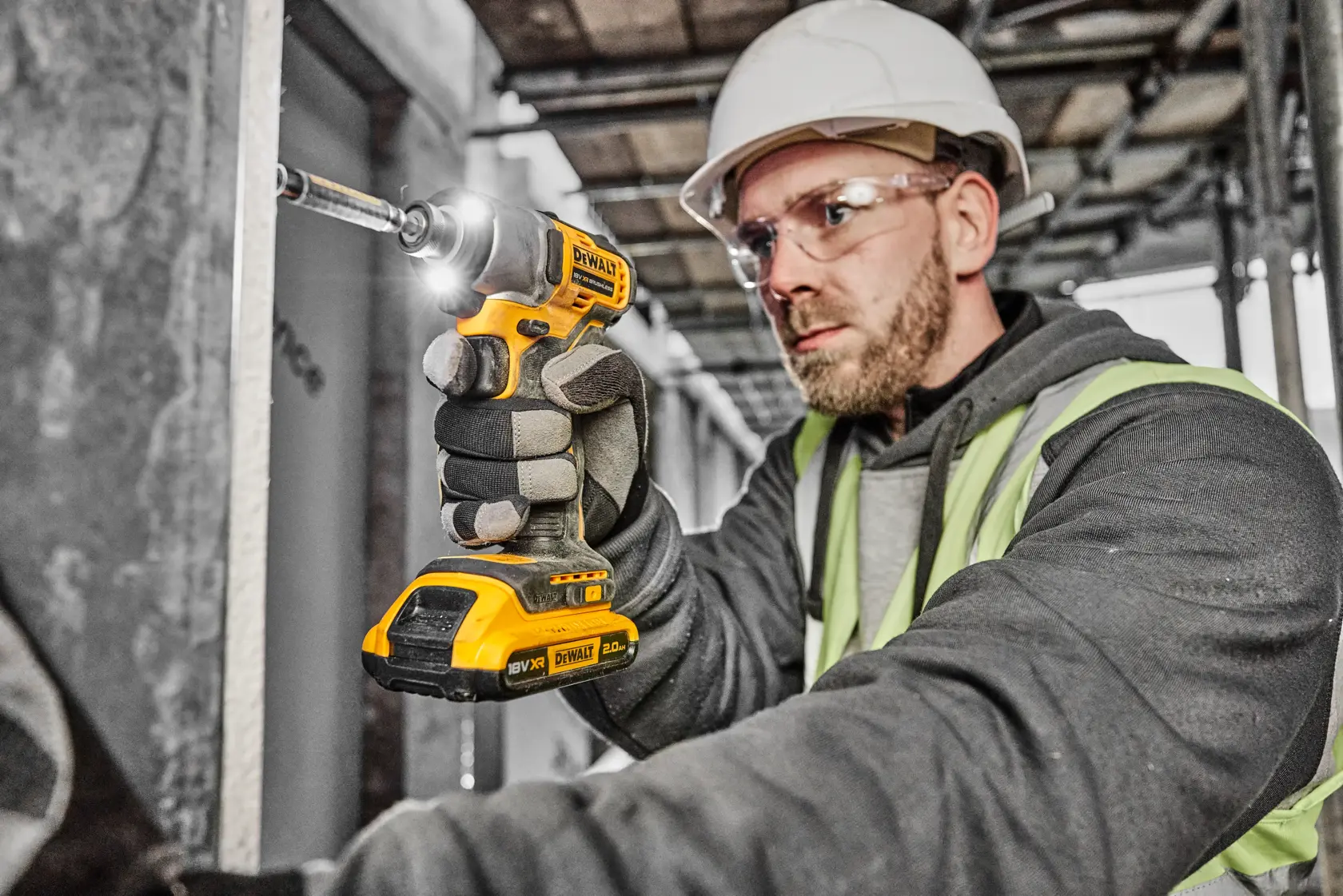 Una persona con casco protettivo e gilet di sicurezza utilizza un avvitatore a impulsi a batteria DEWALT (modello DCF840D2T) in un cantiere.