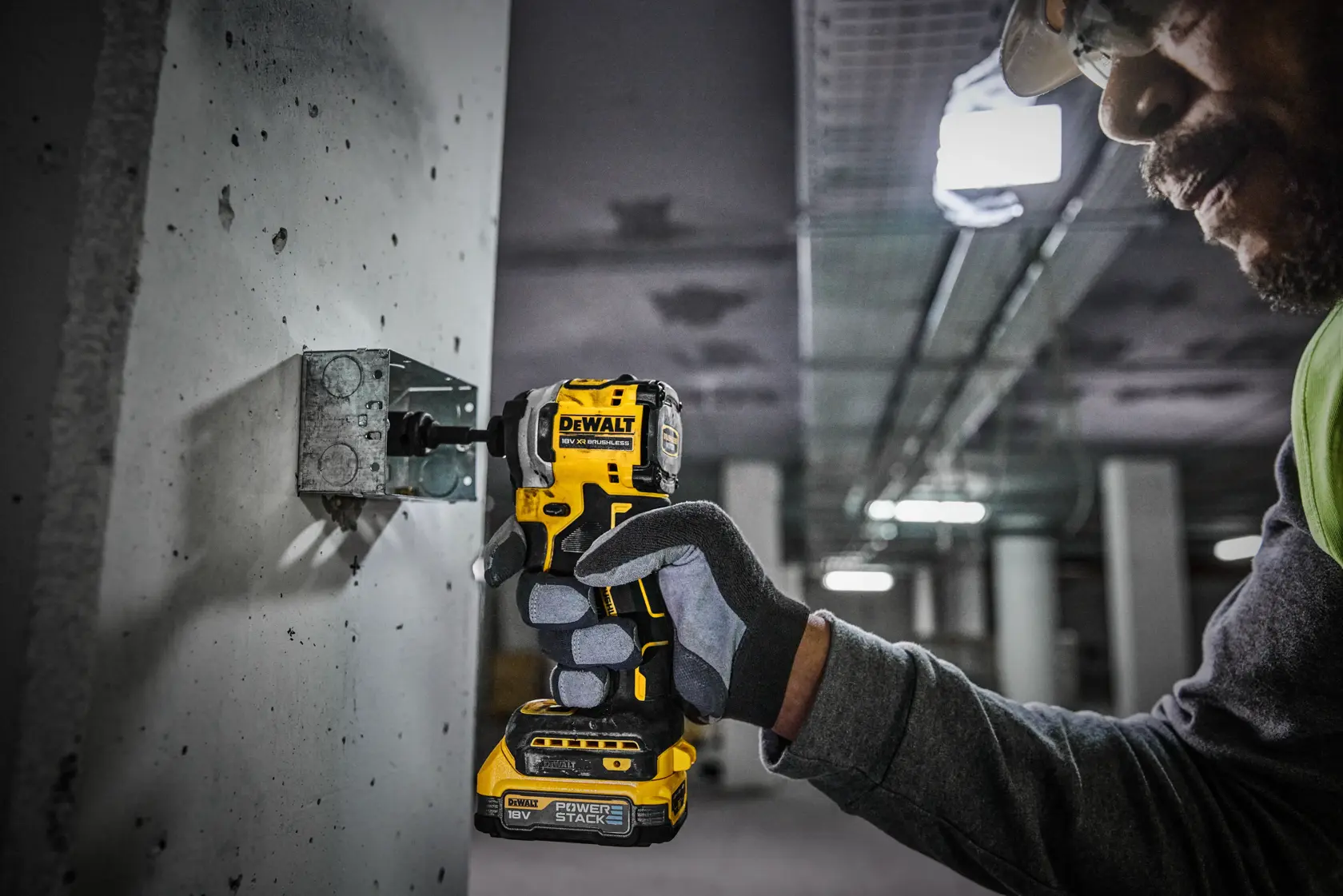 Una persona che indossa guanti di sicurezza utilizza un avvitatore a impulsi a batteria DEWALT (modello DCF850) per fissare una vite in una parete di cemento in un ambiente industriale o edilizio.