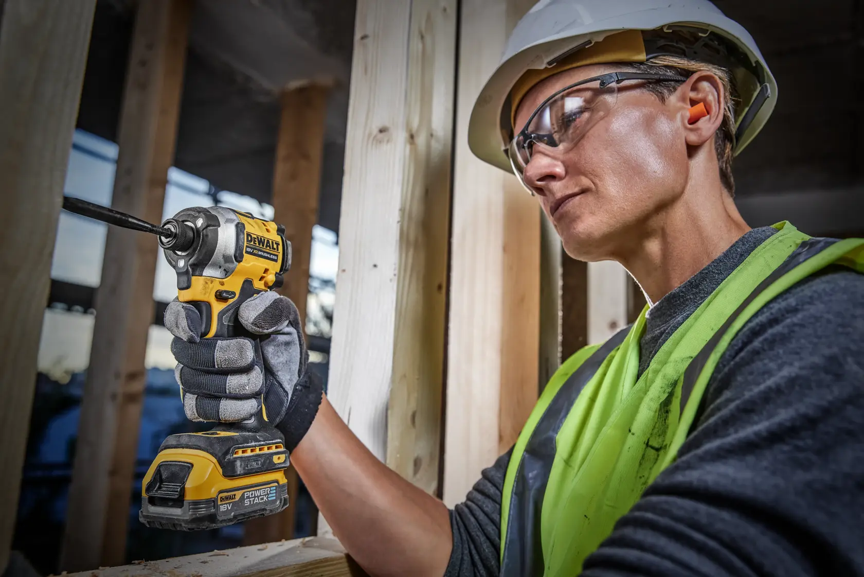 Persona con casco protettivo e giubbotto ad alta visibilità che utilizza un utensile elettrico a batteria DEWALT, nello specifico un avvitatore ad impulsi, su un cantiere edile.