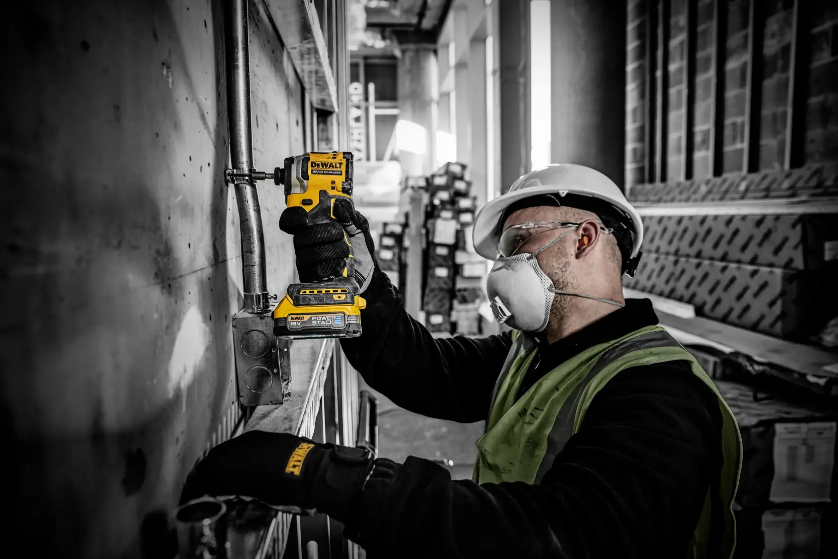 Operaio usa un avvitatore DEWALT DCF850E2T su tubi, con guanti e protezioni, in cantiere.