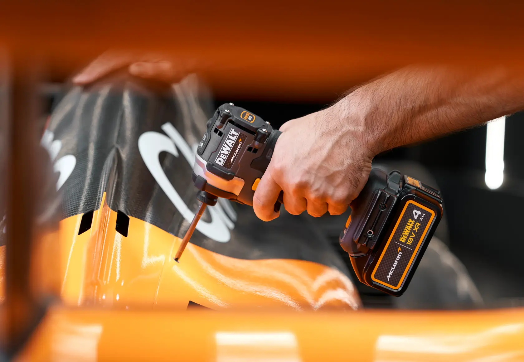 Hand using a DEWALT cordless impact driver on a black and orange surface.