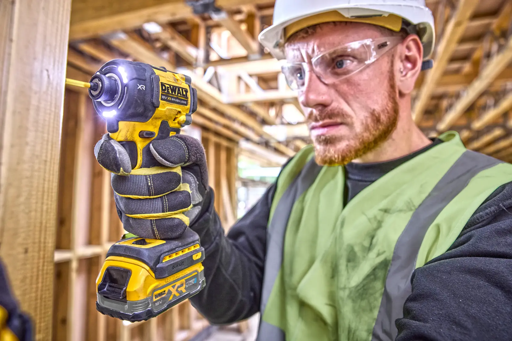 Worker using a DEWALT DCF870E2T impact driver with gloves at a construction site. Face is blurred for privacy.