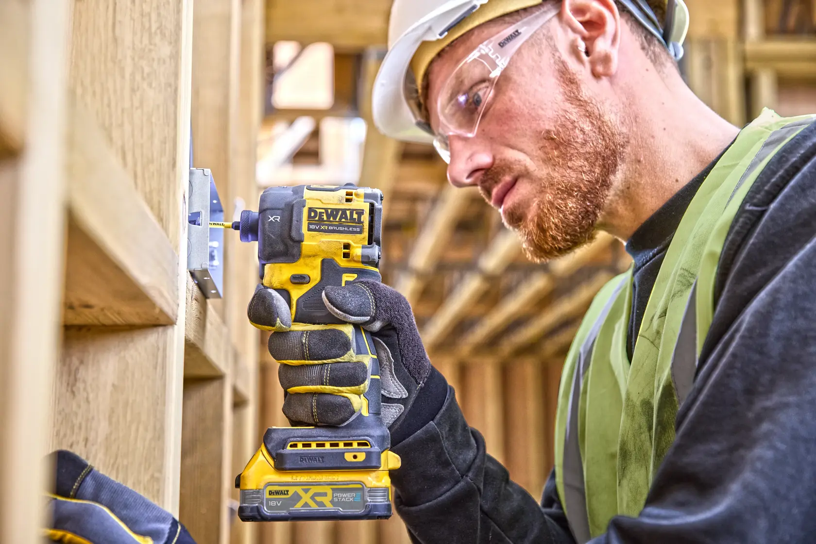 Worker using a DEWALT DCF870N impact driver on wood framing at a construction site.