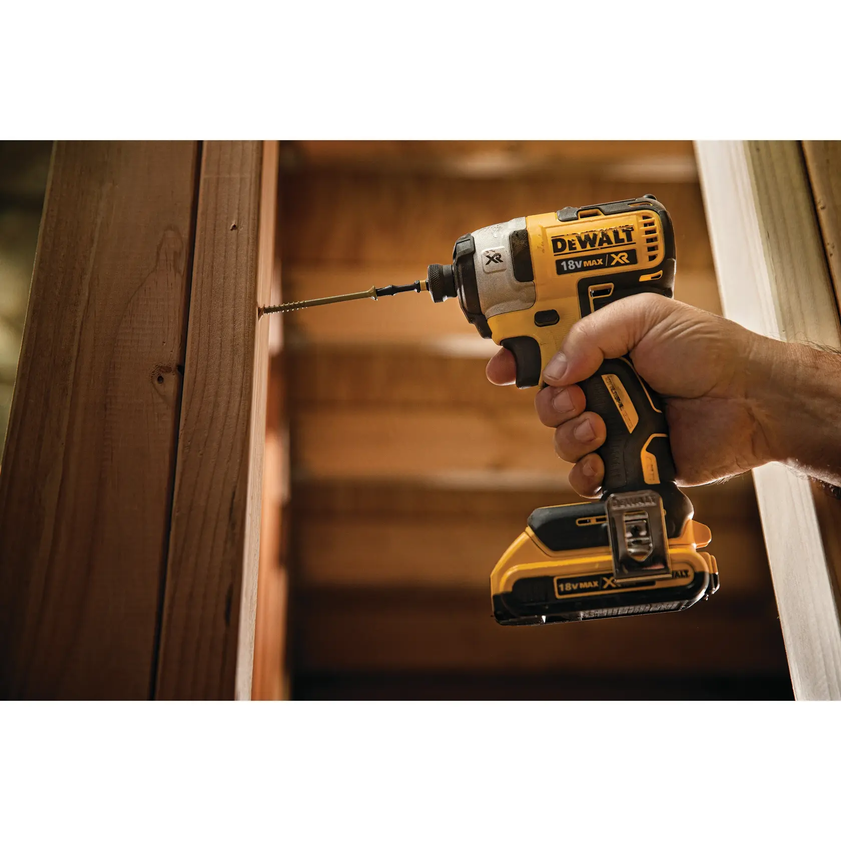 Una mano tiene un avvitatore a impulsi DEWALT 18V senza fili mentre avvita una vite in una trave di legno.