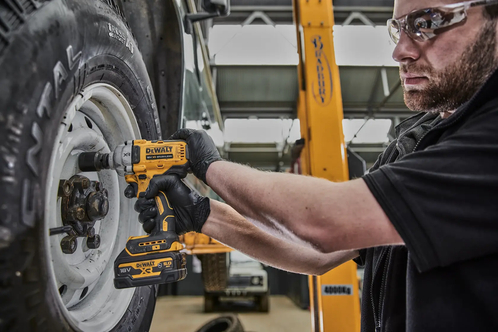 Person uses DEWALT DCF891NT impact wrench to tighten bolts on a vehicle wheel in a garage setting.