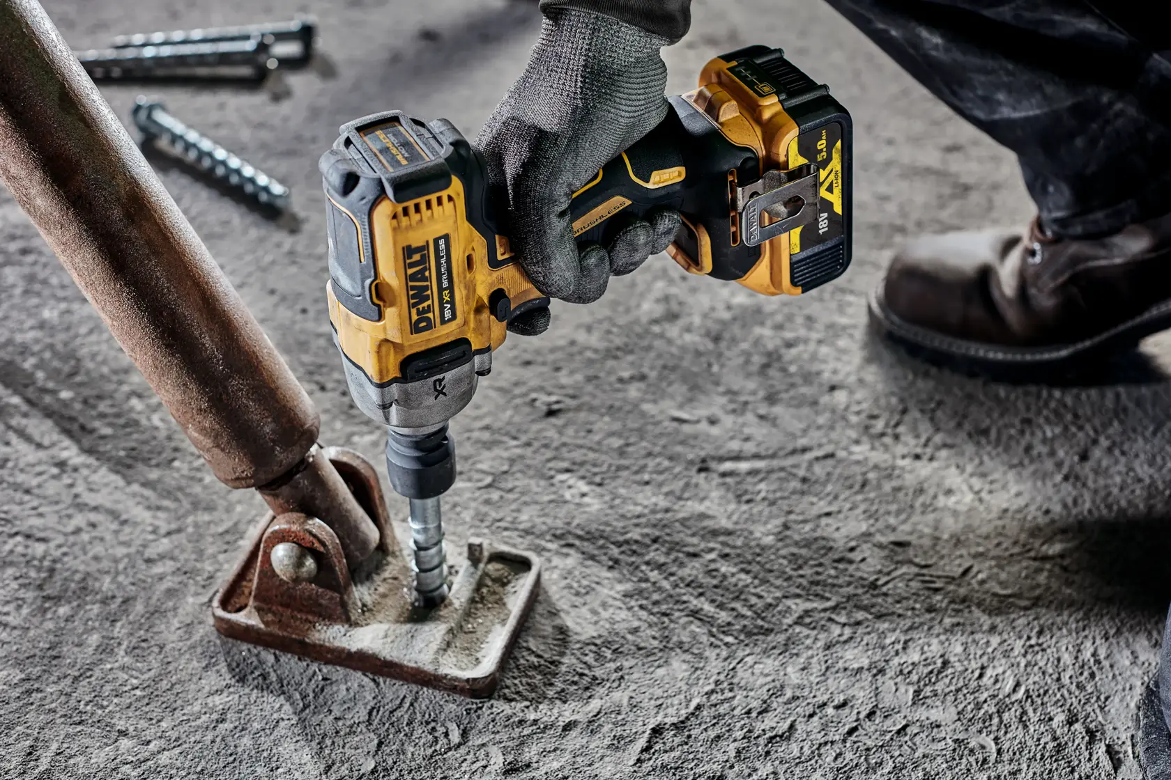 Gloved hand using DEWALT cordless impact wrench on a metal bracket fixed to a concrete floor.