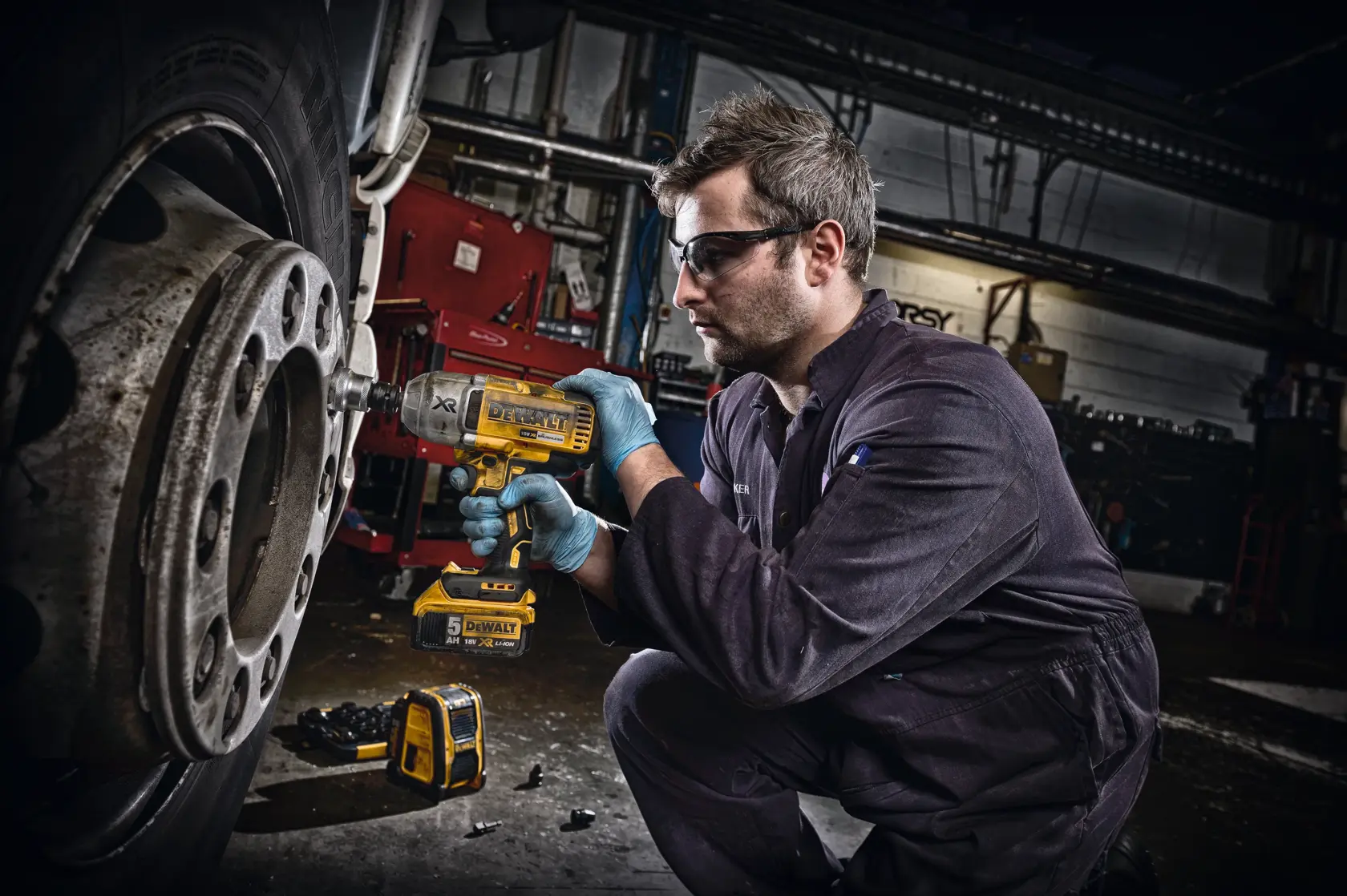 Person uses a DEWALT impact wrench to work on a large vehicle wheel in an industrial workshop.