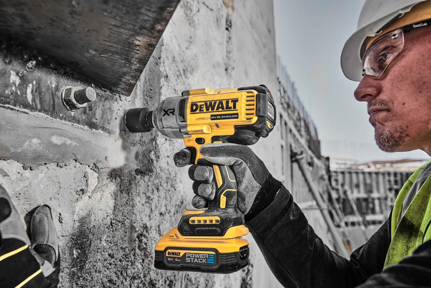 Worker using a DEWALT DCF900H2T drill on a steel beam at a construction site, wearing safety gear and helmet.