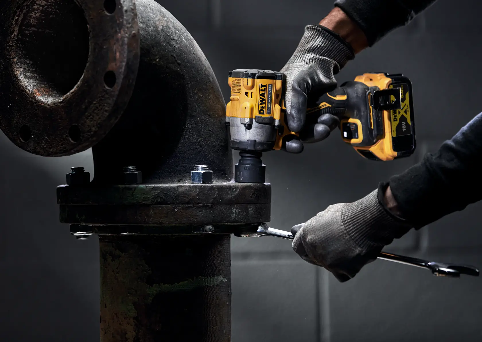 Una persona che indossa guanti da lavoro utilizza un avvitatore a impulsi a batteria DEWALT DCF922P2T per serrare i bulloni di un giunto di tubo industriale.