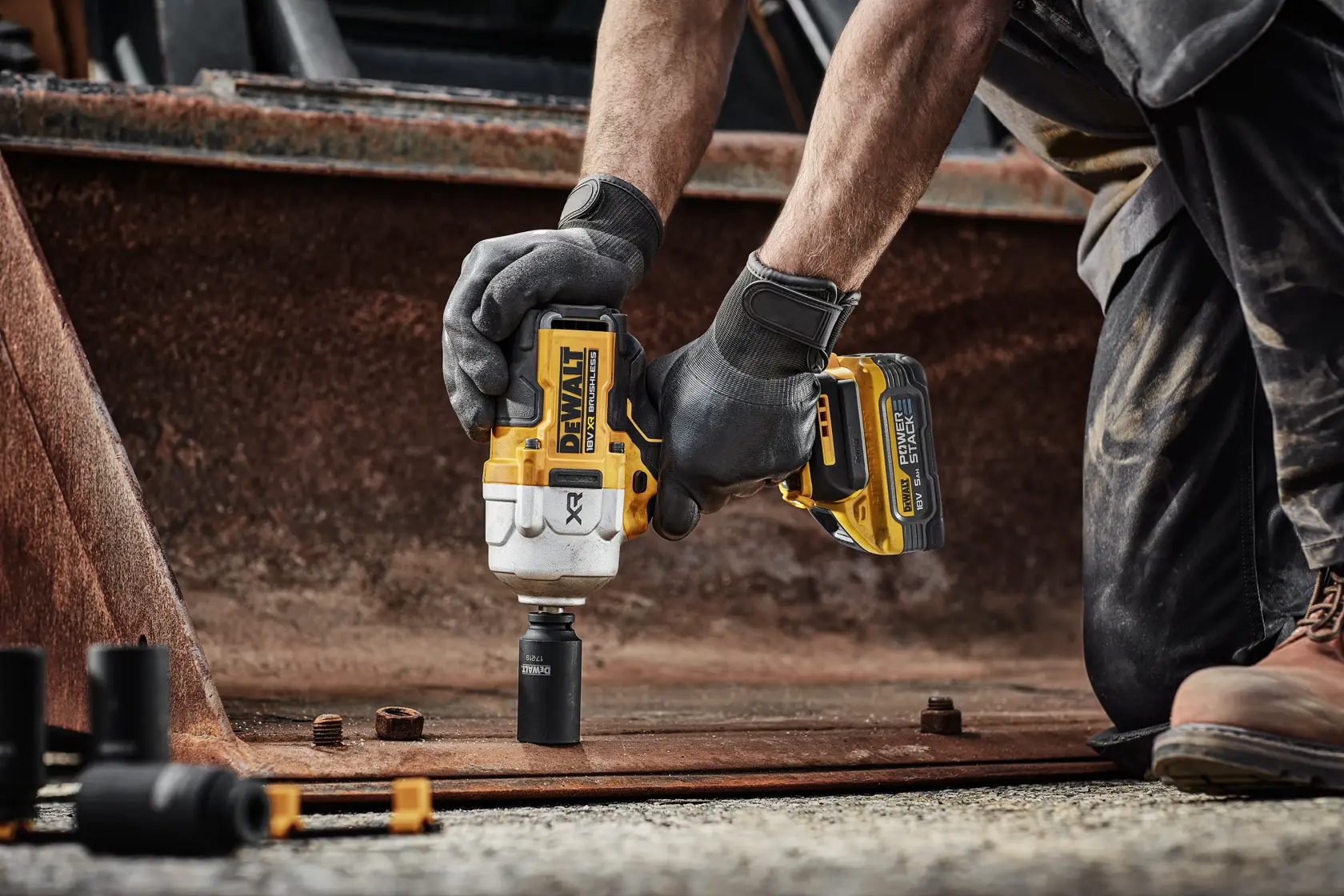 A DEWALT DCF961H2T impact wrench in use on rusty metal, held by a person wearing gloves outdoors.