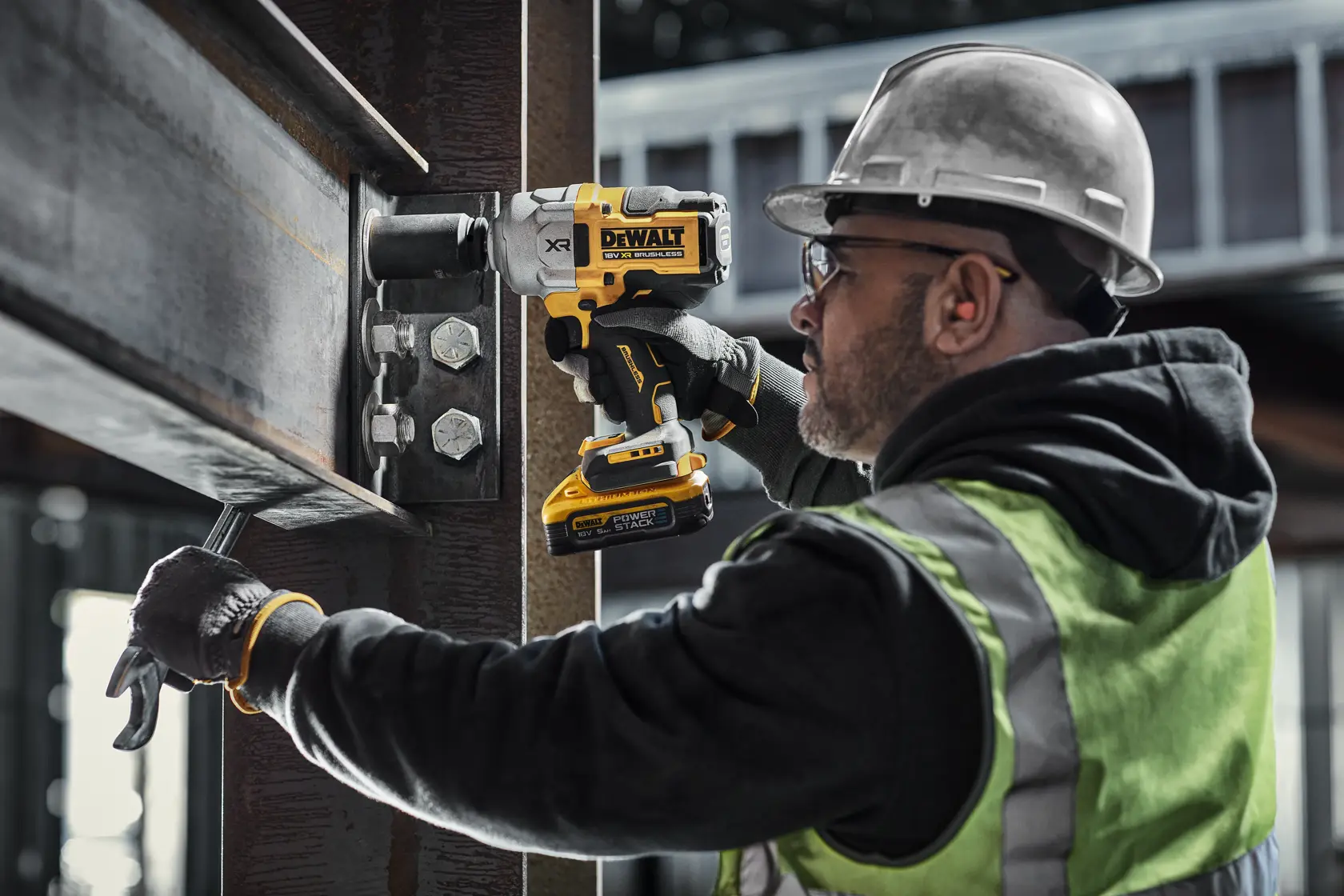 Person uses DEWALT impact wrench to tighten bolts on steel beam at a construction site.