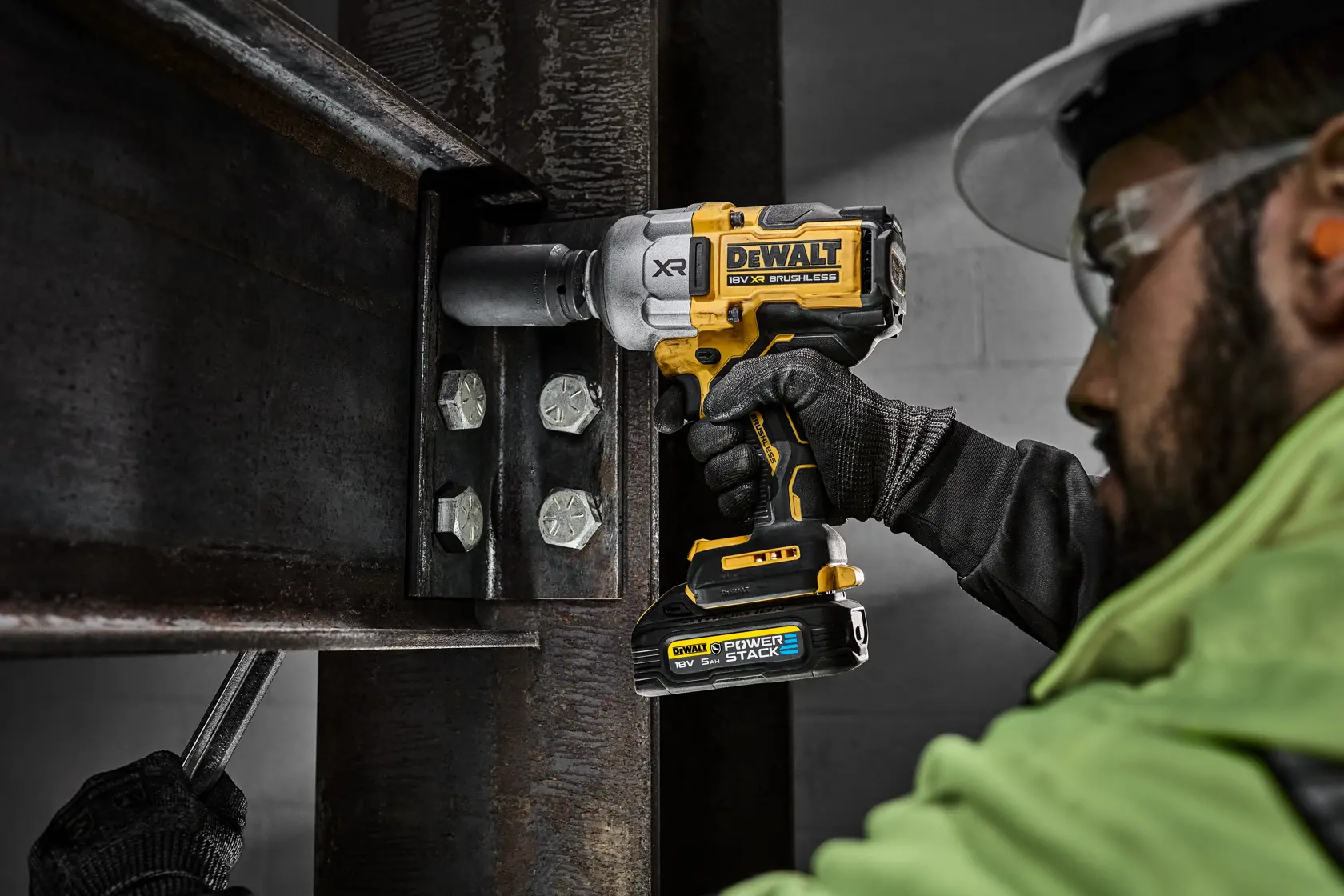 Worker using DEWALT cordless impact wrench on steel beam bolts at a construction site.