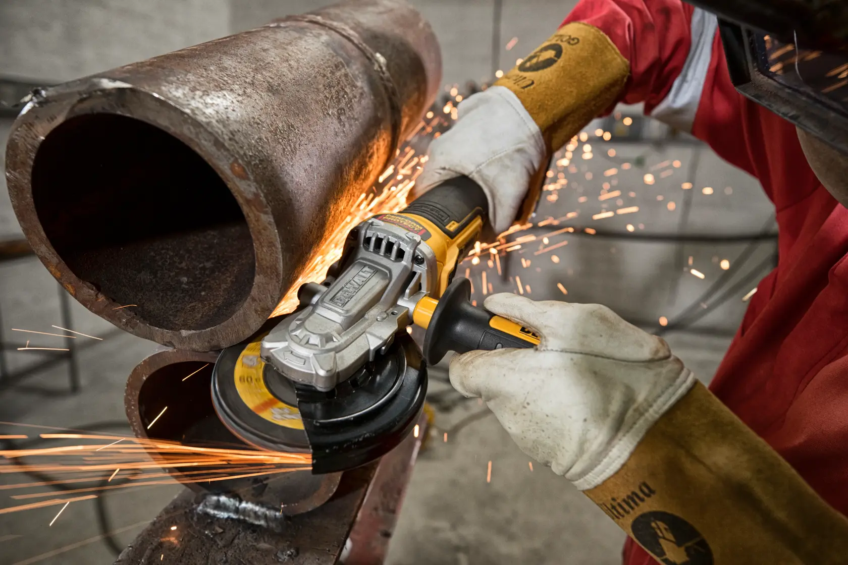 Person uses a DEWALT angle grinder to cut a metal pipe, creating sparks in an industrial setting.