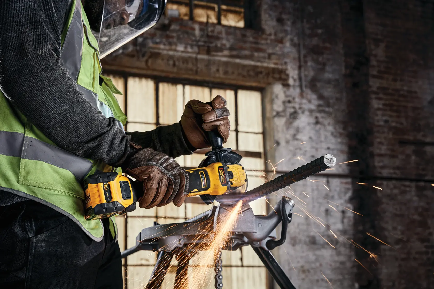 A DEWALT cordless grinder cutting metal, sparks flying, worker wears gloves and safety gear in industrial setting.